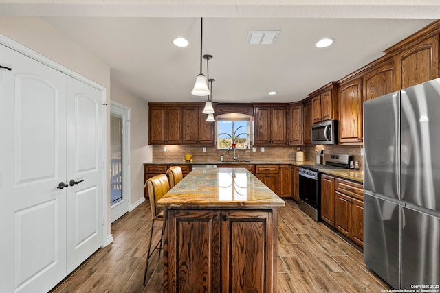 kitchen with a kitchen island, appliances with stainless steel finishes, sink, hanging light fixtures, and light stone counters