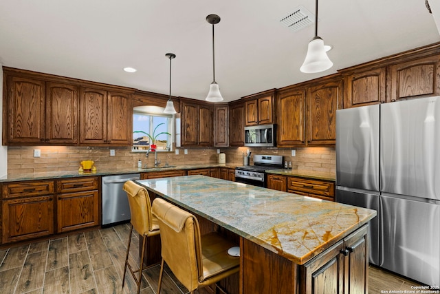 kitchen with sink, appliances with stainless steel finishes, hanging light fixtures, a center island, and light stone countertops