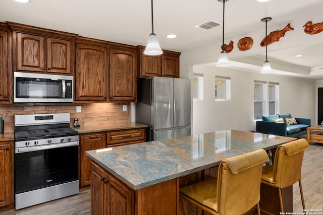 kitchen with light stone counters, appliances with stainless steel finishes, a kitchen breakfast bar, a kitchen island, and backsplash