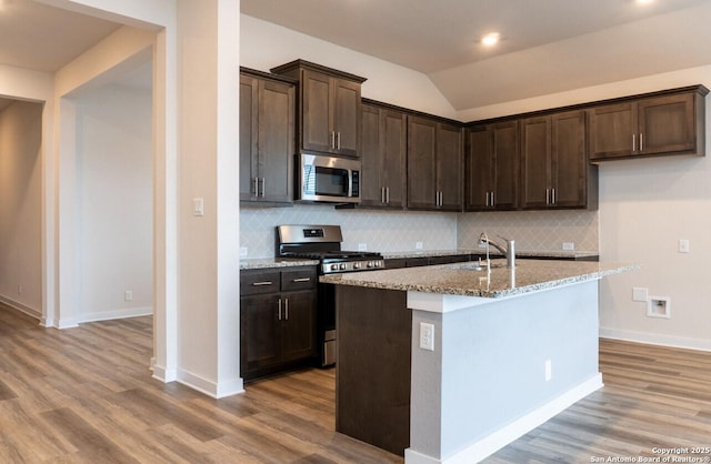 kitchen with a kitchen island with sink, sink, stainless steel appliances, light stone counters, and lofted ceiling