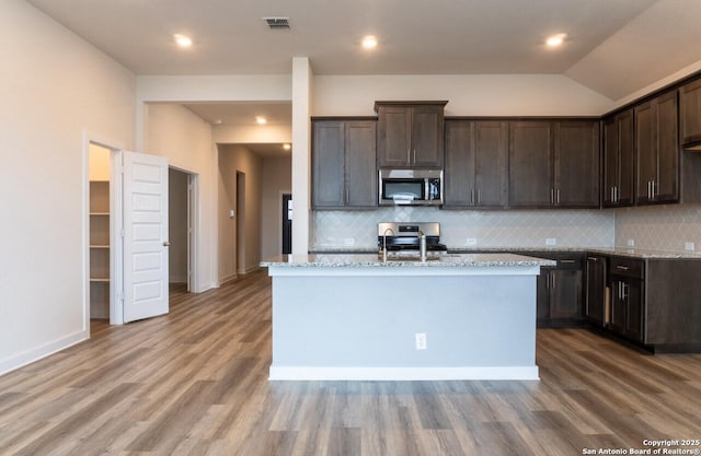 kitchen featuring tasteful backsplash, an island with sink, stainless steel appliances, and vaulted ceiling