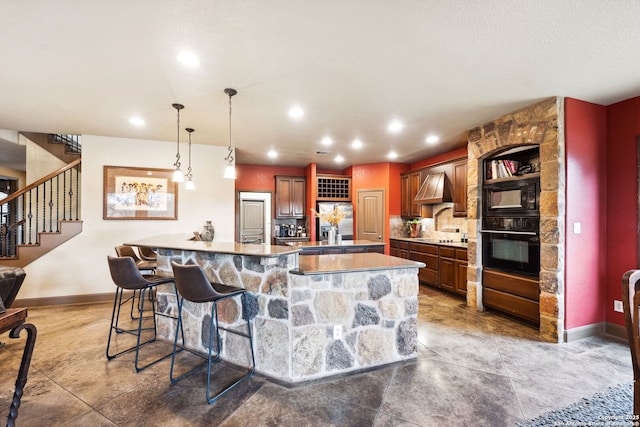 kitchen with black appliances, decorative light fixtures, wall chimney range hood, decorative backsplash, and a breakfast bar area