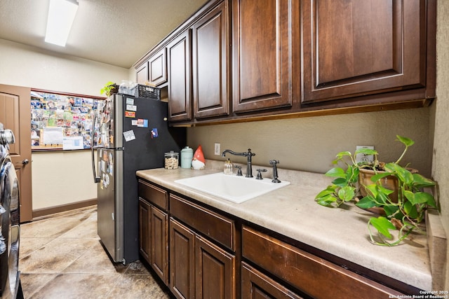 kitchen with sink, dark brown cabinetry, and stainless steel refrigerator