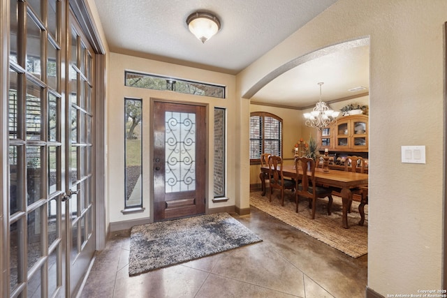 foyer with dark tile patterned flooring, a textured ceiling, a notable chandelier, and ornamental molding