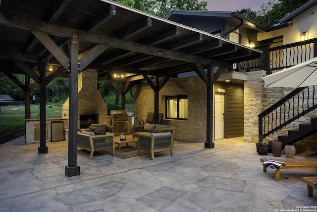 patio terrace at dusk with area for grilling and an outdoor living space with a fireplace