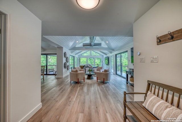 living room with vaulted ceiling with beams, a wealth of natural light, and light hardwood / wood-style flooring