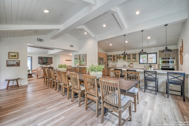 dining room with a healthy amount of sunlight, sink, beam ceiling, and light hardwood / wood-style flooring