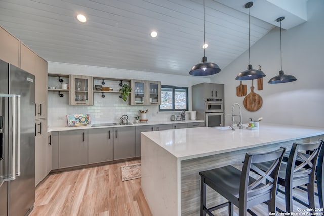 kitchen featuring sink, a breakfast bar area, hanging light fixtures, appliances with stainless steel finishes, and light hardwood / wood-style floors