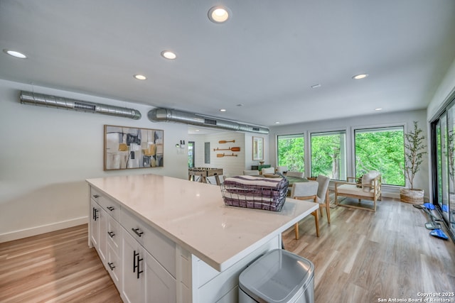 kitchen with light hardwood / wood-style flooring, light stone countertops, a center island, and white cabinets