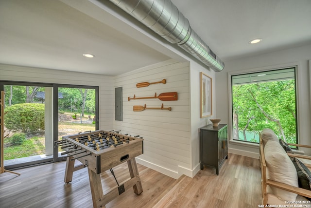 playroom featuring a healthy amount of sunlight, electric panel, light hardwood / wood-style floors, and wood walls