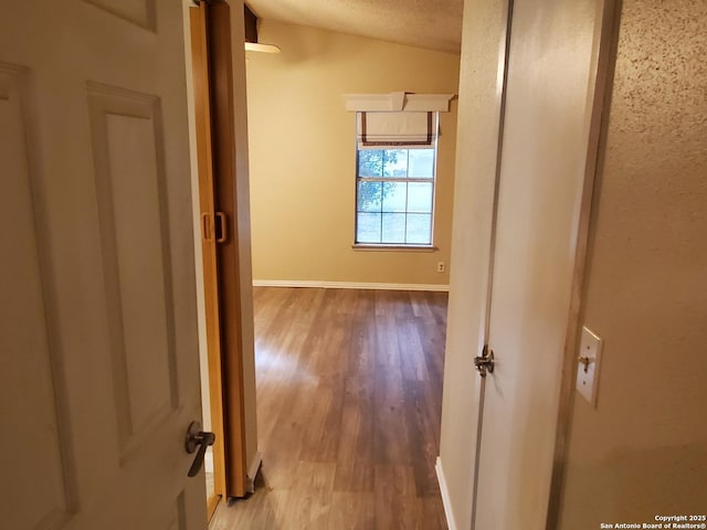 hall featuring lofted ceiling, a textured ceiling, and light hardwood / wood-style floors