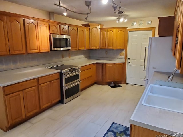 kitchen with sink, decorative backsplash, stainless steel appliances, and rail lighting