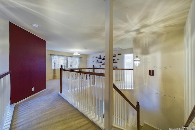 hall featuring a wealth of natural light, an inviting chandelier, and carpet