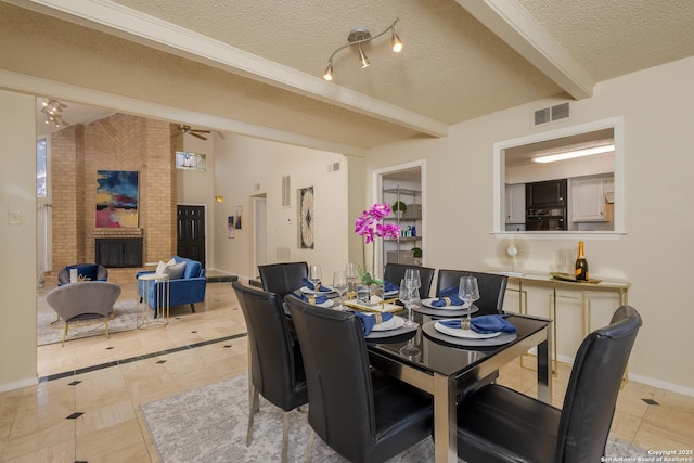 dining space featuring beamed ceiling, a brick fireplace, light tile patterned floors, and a textured ceiling