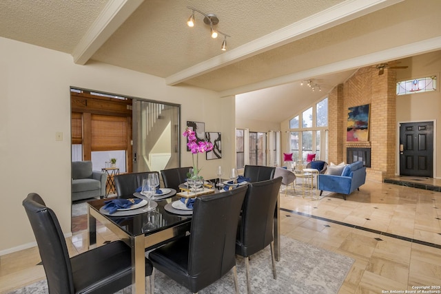 dining room with ceiling fan, a textured ceiling, beamed ceiling, and a brick fireplace