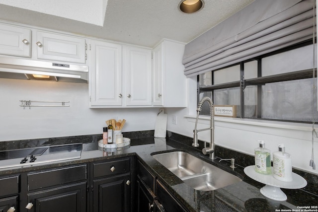 kitchen with a textured ceiling, white cabinetry, black electric stovetop, dark stone counters, and sink