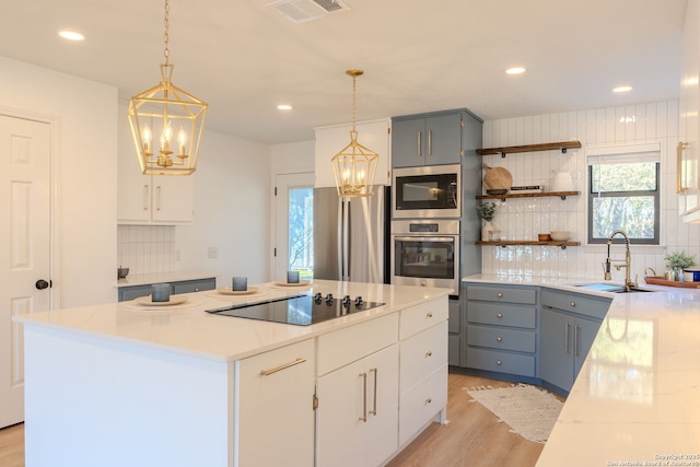 kitchen featuring white cabinets, appliances with stainless steel finishes, a center island, decorative light fixtures, and sink