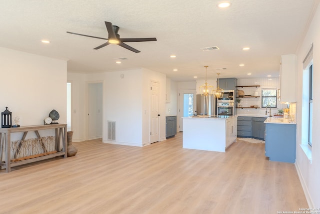 kitchen with white cabinets, appliances with stainless steel finishes, a center island, hanging light fixtures, and light hardwood / wood-style flooring