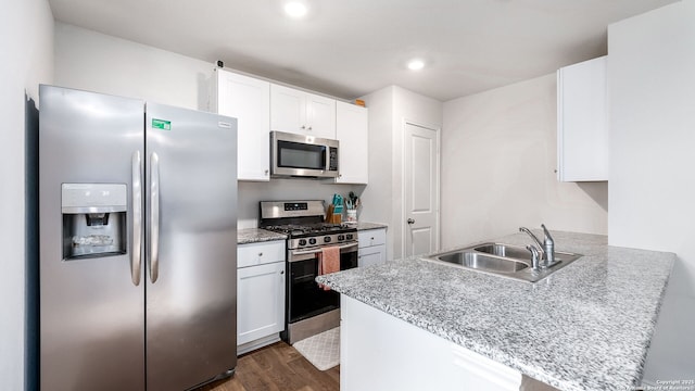 kitchen with kitchen peninsula, appliances with stainless steel finishes, sink, dark wood-type flooring, and white cabinetry