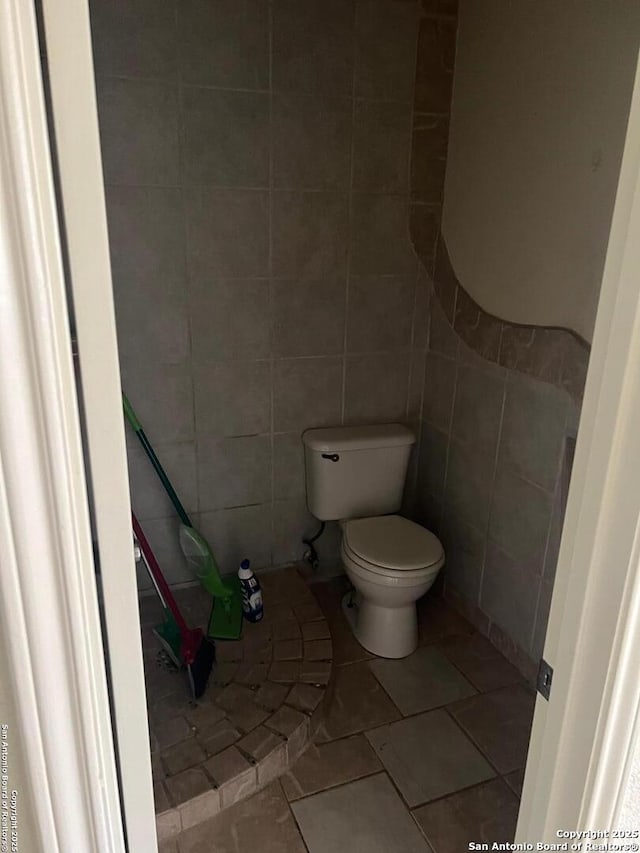 bathroom featuring toilet, tile patterned floors, and tile walls