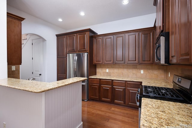 kitchen with dark brown cabinetry, light stone counters, light wood-type flooring, stainless steel appliances, and decorative backsplash