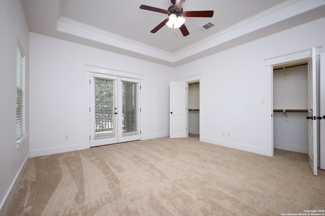 unfurnished bedroom featuring ceiling fan, ornamental molding, a tray ceiling, and light carpet