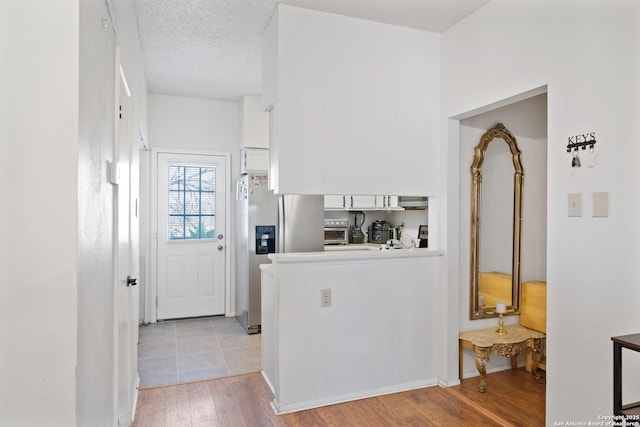 kitchen featuring kitchen peninsula, stainless steel fridge, white cabinets, light wood-type flooring, and a textured ceiling