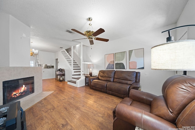 living room featuring a fireplace, a textured ceiling, ceiling fan with notable chandelier, and light wood-type flooring