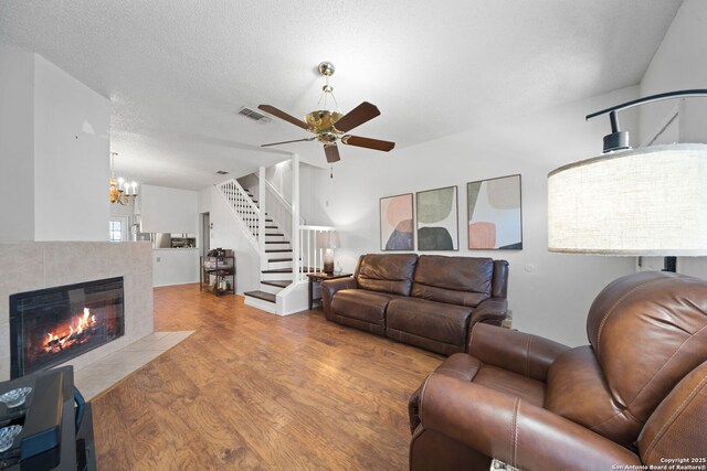 living room with ceiling fan with notable chandelier, a tile fireplace, light hardwood / wood-style floors, and a textured ceiling