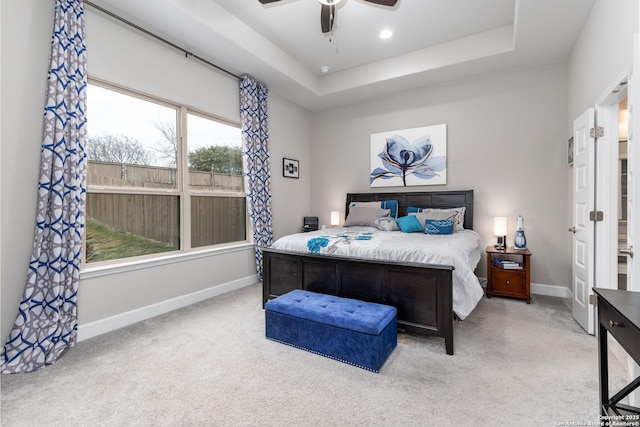 bedroom with ceiling fan, light carpet, and a tray ceiling