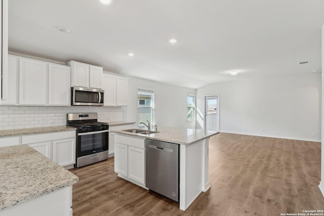 kitchen featuring white cabinets, appliances with stainless steel finishes, sink, vaulted ceiling, and a center island with sink