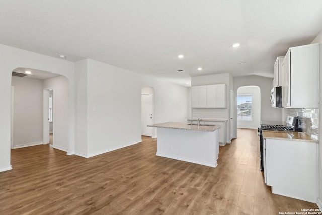 kitchen with white cabinets, a kitchen island with sink, decorative backsplash, and appliances with stainless steel finishes