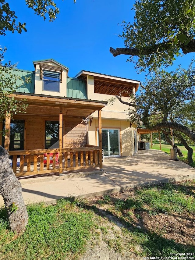 view of front facade with stucco siding, covered porch, a patio area, and metal roof