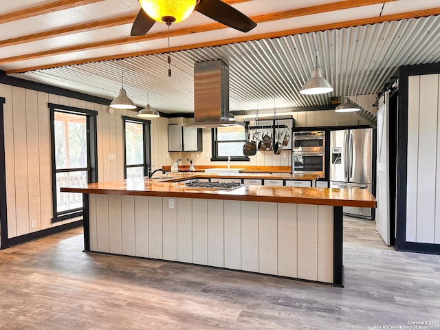 kitchen with appliances with stainless steel finishes, decorative light fixtures, wood walls, island exhaust hood, and light hardwood / wood-style flooring