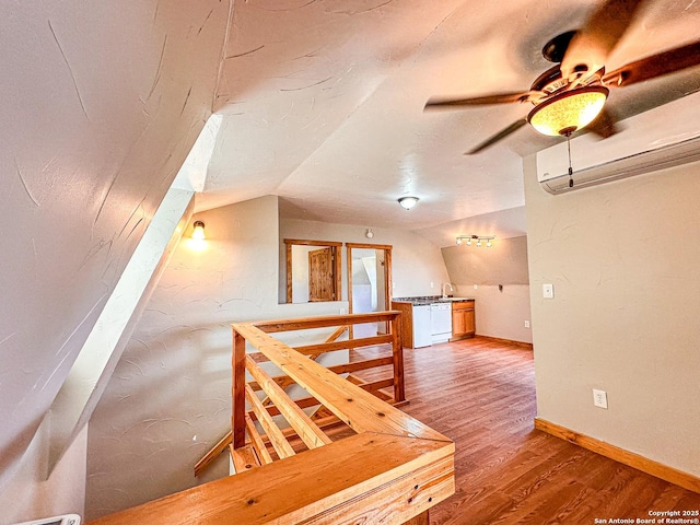 interior space with wood-type flooring, lofted ceiling, a wall mounted air conditioner, and ceiling fan