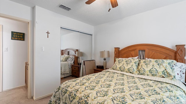 bedroom with light carpet, visible vents, ceiling fan, a textured ceiling, and a closet