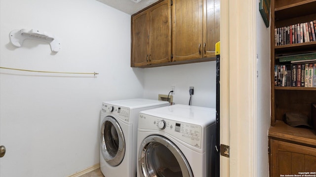 washroom featuring washing machine and dryer, cabinet space, and baseboards