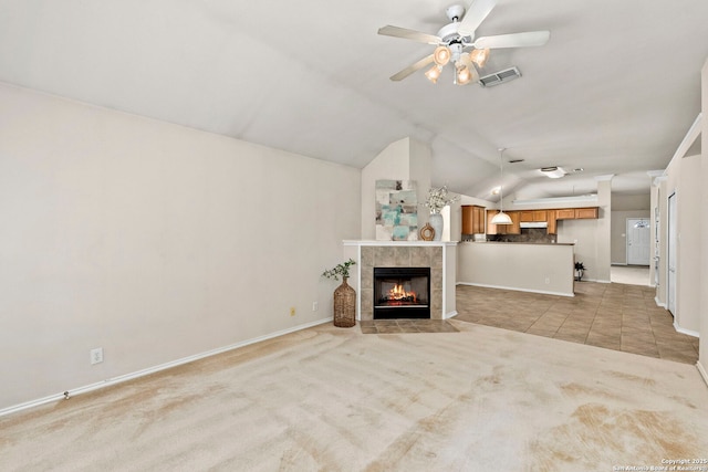 unfurnished living room with light carpet, a tiled fireplace, vaulted ceiling, and ceiling fan