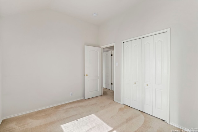 unfurnished bedroom featuring a closet, light carpet, and lofted ceiling