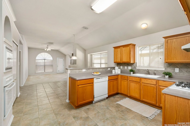 kitchen featuring kitchen peninsula, vaulted ceiling, sink, white appliances, and decorative backsplash