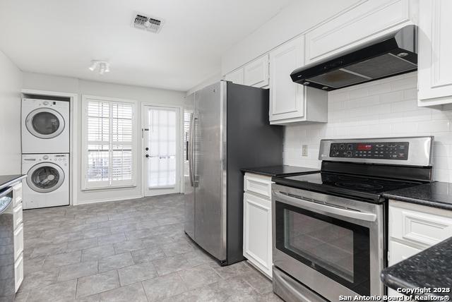 kitchen with white cabinetry, wall chimney range hood, stainless steel appliances, and stacked washing maching and dryer