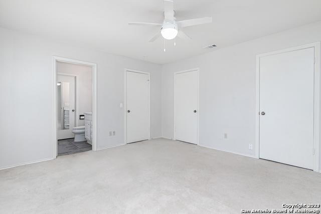 unfurnished bedroom featuring light colored carpet, ensuite bath, and ceiling fan