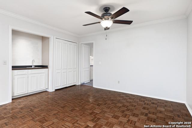 unfurnished bedroom featuring ceiling fan, sink, dark parquet flooring, two closets, and ornamental molding