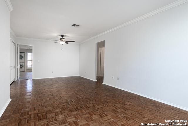 empty room featuring ceiling fan, crown molding, stacked washing maching and dryer, and dark parquet floors