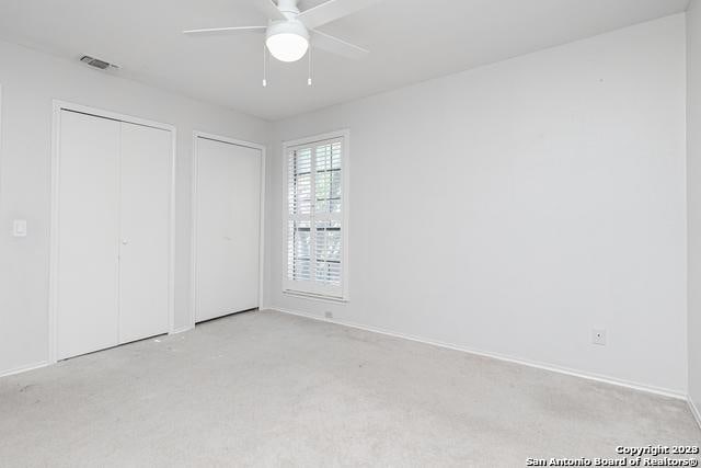 unfurnished bedroom featuring ceiling fan, light carpet, and two closets