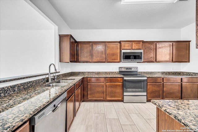 kitchen with a textured ceiling, appliances with stainless steel finishes, dark stone countertops, light hardwood / wood-style floors, and sink