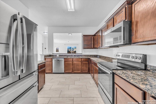 kitchen with sink, a textured ceiling, stainless steel appliances, and dark stone countertops