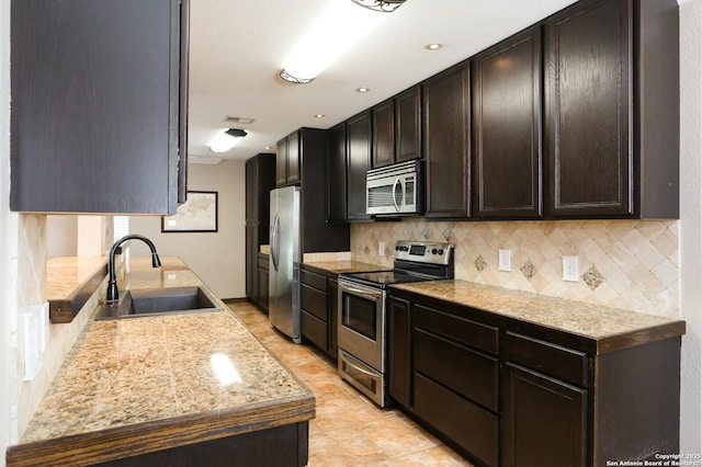 kitchen with dark brown cabinetry, sink, tasteful backsplash, light stone counters, and stainless steel appliances