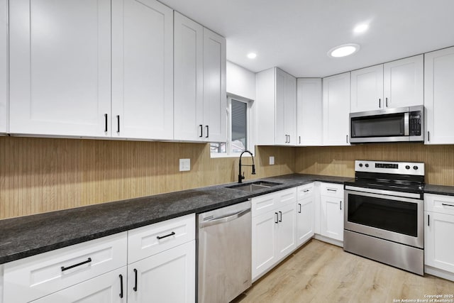 kitchen featuring appliances with stainless steel finishes, sink, light wood-type flooring, white cabinetry, and dark stone countertops