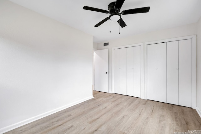 unfurnished bedroom featuring ceiling fan, two closets, and light wood-type flooring